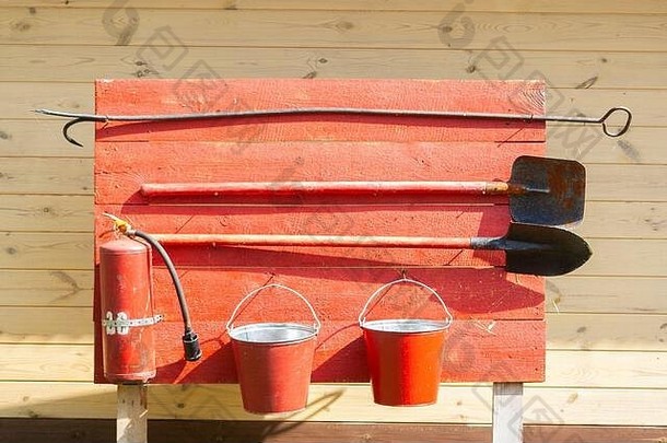 红色木板上的一套<strong>消防安全</strong>仪表。灭火器、水桶、废料和铲子。