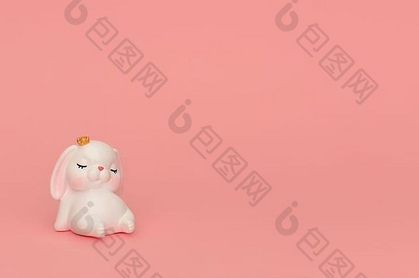 粉色背景上戴着皇冠睡觉的可爱兔子。白色吉祥物玩具睡兔和粉红色的耳朵坐在粉红色。横幅、邀请、儿童餐。