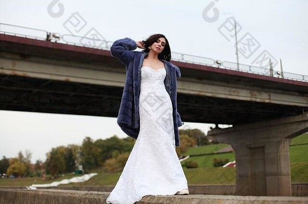 都市时尚<strong>婚纱摄影</strong>，新娘穿着紫色貂皮大衣外出，站在桥旁，低角度观看，广告理念。