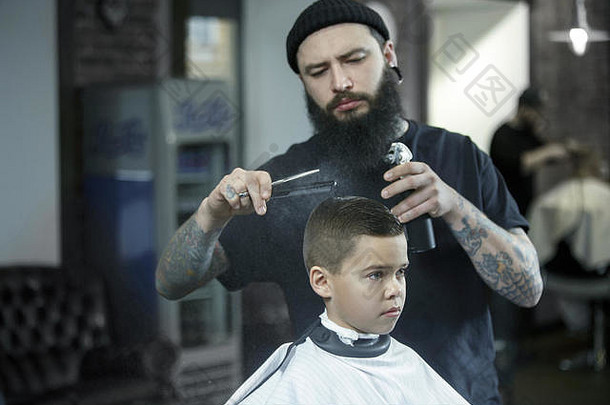 <strong>儿童</strong>理发师在黑暗的背景下给小男孩理发。心满意足的可爱学龄前男孩正在理发。