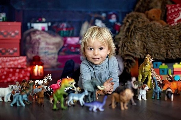 可爱的金发小男孩，在家里玩塑料动物和恐龙，圣诞装饰围绕着他