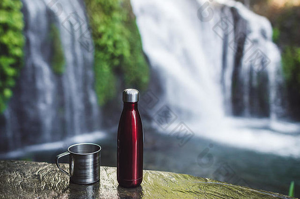 红色的热水瓶瓶钢杯背景热带瀑布浪费生态概念徒步旅行设备