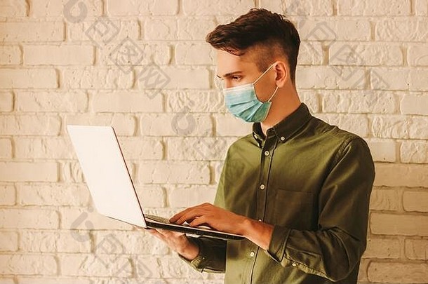 戴着防护面罩，手持笔记本电脑的自由职业者。戴着医用面罩的商人在家里用电脑工作。男人在网上商店购物。