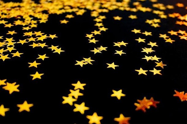 金色的星星五彩纸屑散落在黑色的背景上。创意假日概念。