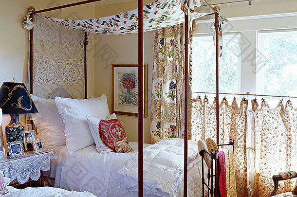 平房卧室的金属四柱床上有花冠，床上有白色枕头和床单，窗户上有花咖啡窗帘