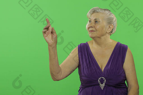 一位老妇人指着什么东西笑了。穿着紫色连衣裙的漂亮老奶奶。放置您的徽标或文字。色度键。绿色屏幕背景