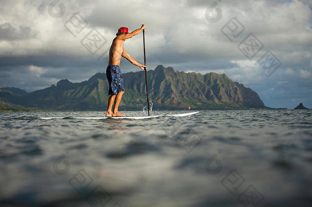 从卡尼奥赫湾的晨起划桨板会议上看去，日出时布拉德·奥斯本在热带混合划桨板上划桨。
