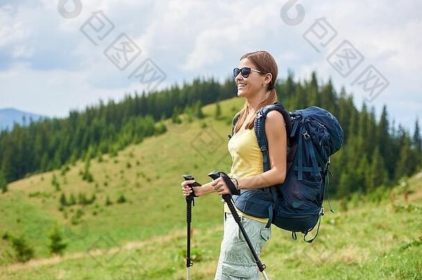 美丽快乐的女背包客在喀尔巴阡山路徒步旅行，在青草丛生的小山上行走，背着背包，使用<strong>登山杖</strong>，享受夏日。户外活动、旅游理念