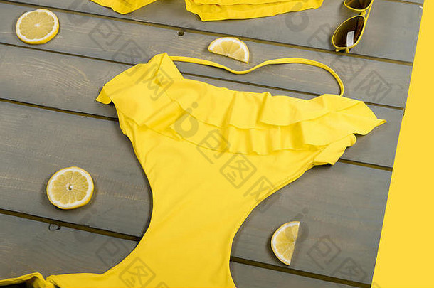 黄色泳衣一体式，泳裤，飞行员太阳镜，柠檬色灰色木板。木制背景上的海滩配件。