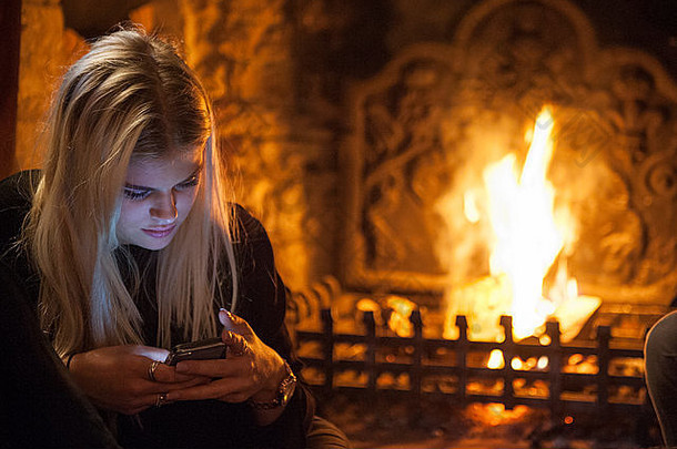 冬天，一个女孩坐在<strong>熊熊大火</strong>前检查她的手机。电话照亮了她的脸。