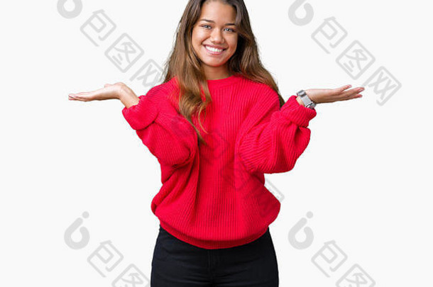 年轻漂亮的黑发女子，穿着红色冬季毛衣，在孤立的背景下微笑着双手张开手掌，展示并宣传c