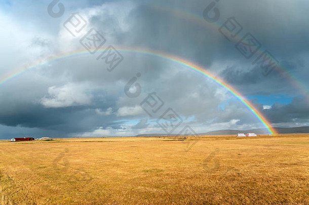 秋天，在冰岛乡村的草地上，彩虹映衬着暴风雨的天空