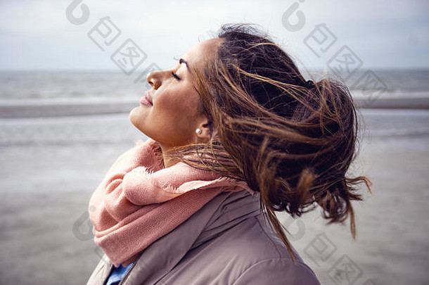 海滩上，戴着围巾的年轻漂亮女模特，头发被风吹过。