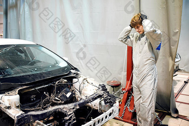 在维修车库里，身穿白色制服的机械师把头靠在汽车上