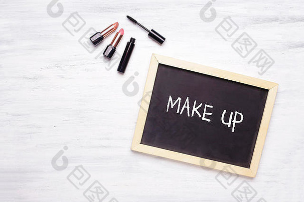 黑板上写着化妆品，白色木质背景上有化妆品。时尚与化妆理念。