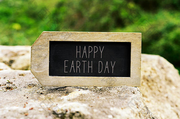 在背景为风景的岩石上，贴上标签形状的黑板，上面写着“地球日快乐”