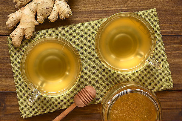 热姜茶装在玻璃杯中，旁边放着蜂蜜和生姜，用自然光照在头顶的木头上