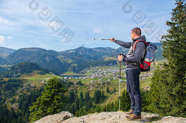 徒步旅行者——背着背包和登山杖的年轻人站在悬崖边，看着湖面，后视图