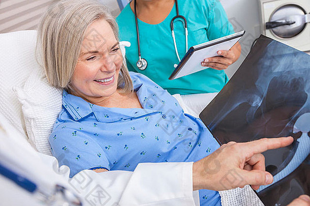 快乐的老年女患者在病床上康复，男医生和女护士正在看髋关节置换术x光片
