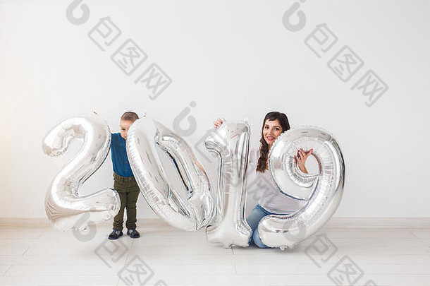 2019年的新年即将来临——母亲和她的儿子坐在室内银色数字旁边。