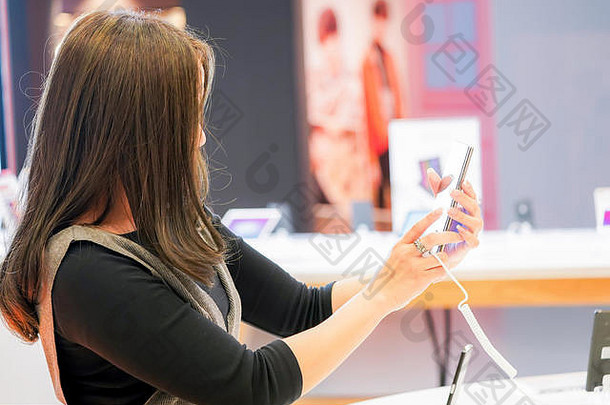 年轻的亚洲女孩在电子<strong>手机店</strong>测试和玩新手机。