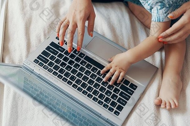 年轻的母亲和她的孩子在家的卧室里用笔记本电脑工作。多任务，自由职业者和母亲的概念。闭合