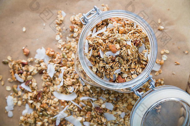 玻璃Jar自制的有机格兰诺拉麦片椰子山核桃烘焙纸背景美味的早餐麦片健康的牛奶什锦早餐