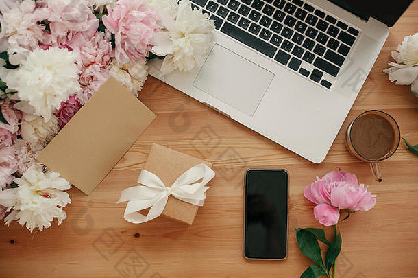 时尚的笔记本电脑、空屏幕手机、礼品盒、咖啡和牡丹花放在质朴的木桌上。文本的空间。国际妇女节。自由的