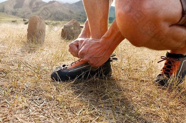 在攀岩训练前，一位面目全非的男子在户外穿上橙色的登山鞋并系上鞋带的特写镜头。