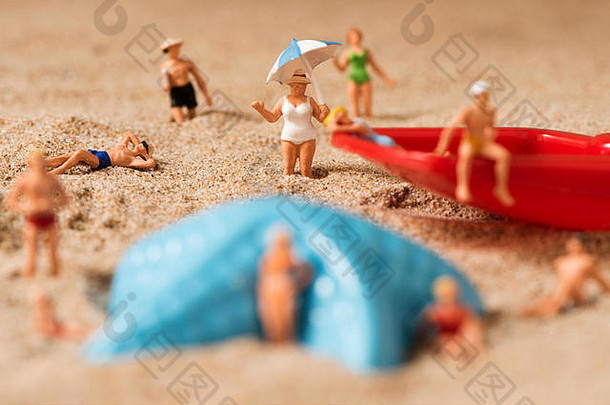 在海滩的沙滩上，一些穿着泳衣的人们在一只蓝色塑料海星和一把红色玩具铲旁放松