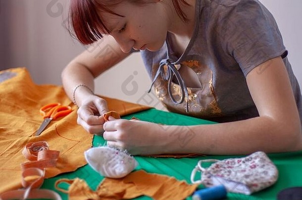 年轻的女裁缝缝口罩的空白。具有欧洲外貌的女孩。制作面具的过程。附近有剪刀和卷尺。