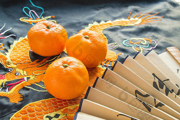 农历新年，橘子和扇子躺在丝绸上绣着龙。