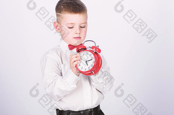 设置闹钟。小男孩抱着红色的钟。是时候了。时间表和时间安排。早上的例行公事。带闹钟的小学生。儿童可爱男孩白色衬衫红结。发展自律。