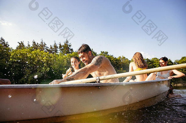 一群快乐的朋友在河里嬉笑和<strong>游泳</strong>。阳光明媚的河畔，穿着泳衣的快乐男女在船上。<strong>夏日</strong>、友谊、度假、周末概念。