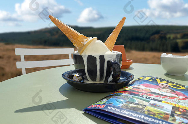 在达特穆尔的阳光下，不想要的德文郡凝块冰激凌蛋卷被扔进卡布奇诺咖啡里，放在花园外的绿色桌子上。