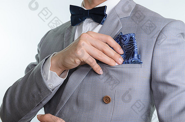 身着灰色西装、格纹面料、蓝色领结和方形口袋、白色背景的男士