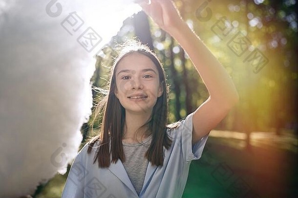 一个美丽的年轻女孩在公园吃棉花糖的肖像