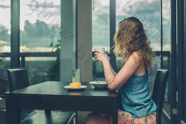年轻的女人坐着表格窗口现代城市公寓早餐