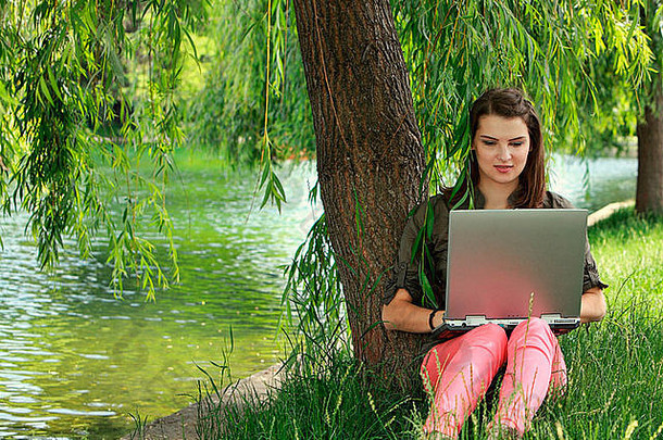 一位年轻漂亮的女士在池塘边的柳树下的公园里学习。
