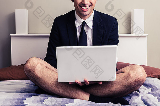 坐在床上拿着笔记本电脑的年轻商人