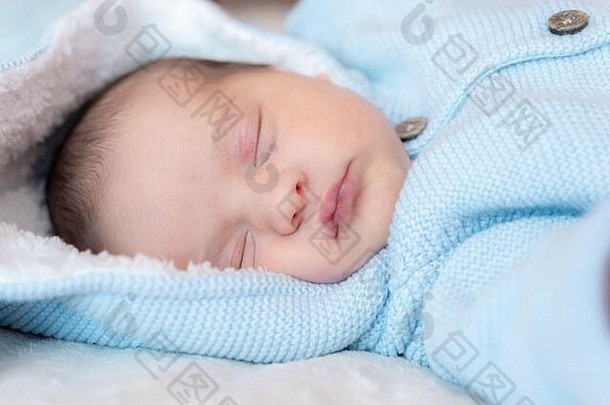 新生儿特写镜头。侧视图：一名新生婴儿穿着蓝色罩衫，头戴兜帽，耳朵在白色背景上，仰面<strong>酣睡</strong>。肖像