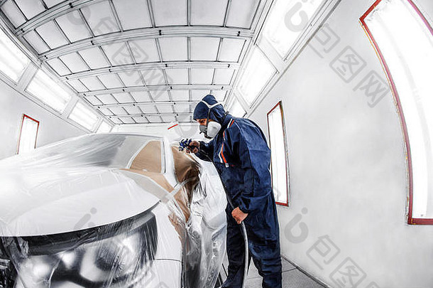 工人在专门的车库里刷白色汽车，穿着服装和防护装备