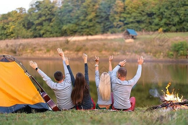 从后面。一群快乐的朋友在河边露营，手挽着手跳舞，欣赏风景。假期很有趣。