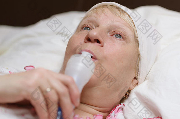 这位老年妇女在家里通过喷雾器进行呼吸治疗。