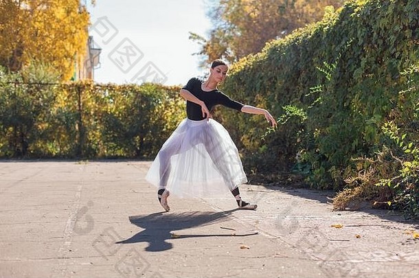 在秋天公园，一位身穿白色芭蕾舞裙、穿着尖头鞋跳舞的女芭蕾舞演员。
