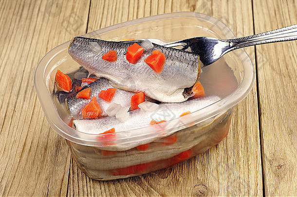 叉子上的腌鱼和木制背景上的塑料罐