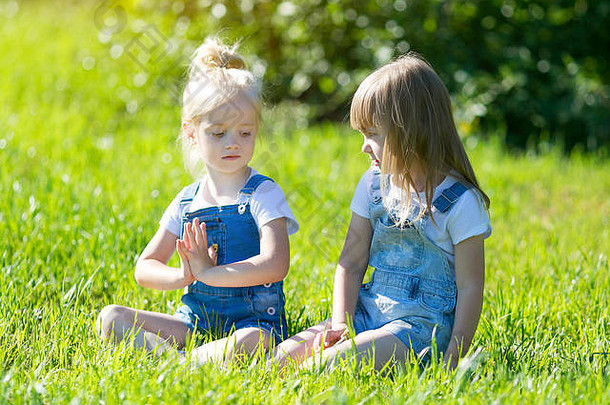 两个小女孩在城市公园的草地上练习运动<strong>瑜伽</strong>。