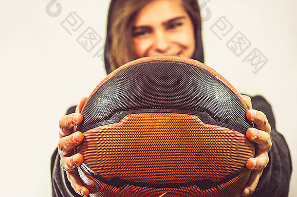 女孩拿着篮球，微笑着。她穿着一件运动连帽衫。照片的暖色很好。