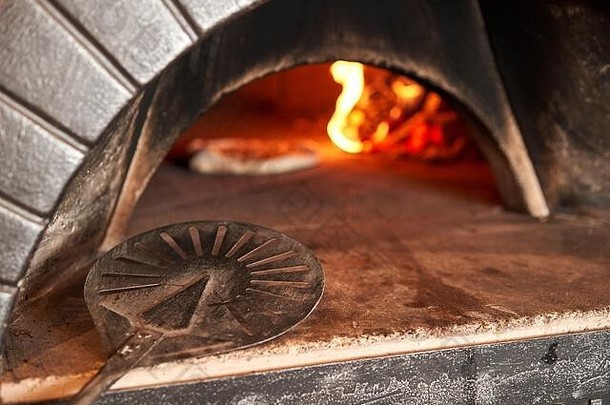 金属铲的特写镜头。意大利那不勒斯餐厅，用传统的木制烤箱烤出美味的玛格丽塔比萨饼。原汁原味的那不勒斯披萨。炽热的煤。
