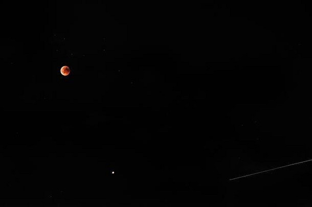 满天繁星的黑色天空中，血红色的月食伴随着彗星的踪迹
